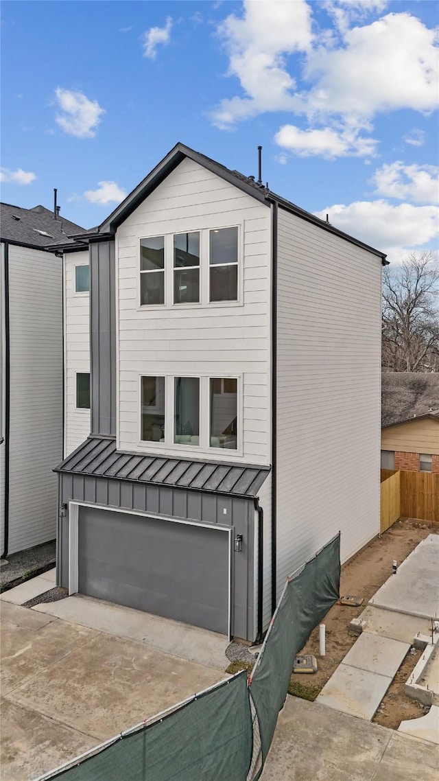 view of front of property with fence, a garage, a standing seam roof, driveway, and metal roof