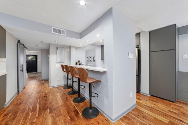 8924 Chatsworth Dr, Houston, TX 77024 - kitchen featuring a barn door, a kitchen breakfast bar, light wood-type flooring, light countertops, and recessed lighting