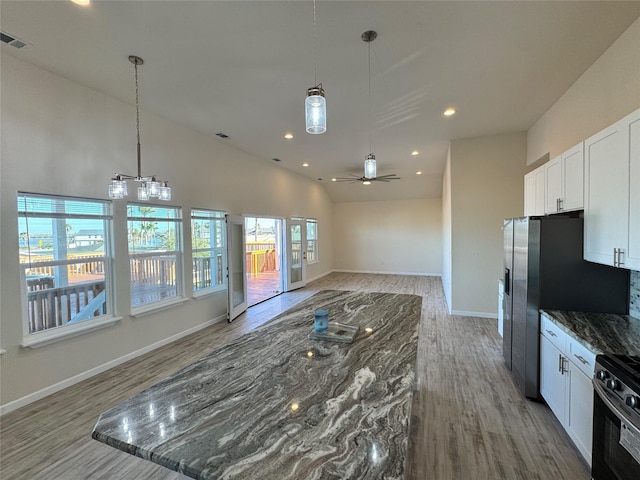 kitchen featuring lofted ceiling, light wood finished floors, open floor plan, white cabinetry, and ceiling fan with notable chandelier