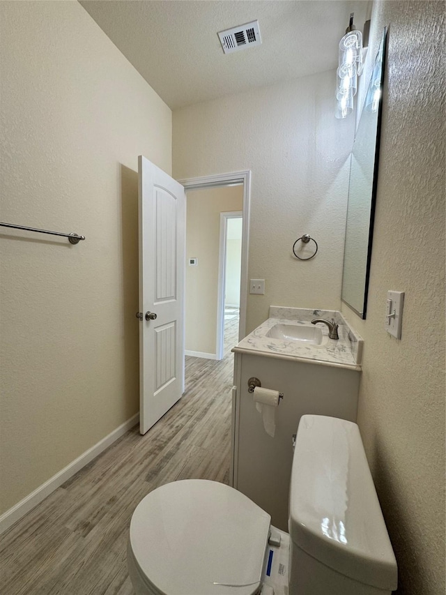 half bathroom with toilet, wood finished floors, a sink, baseboards, and visible vents