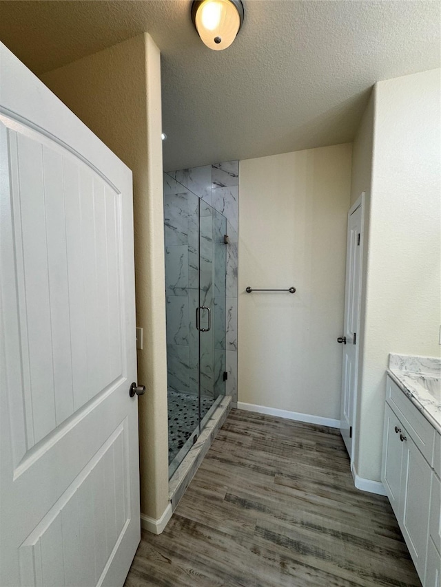bathroom with a marble finish shower, a textured ceiling, baseboards, wood finished floors, and vanity
