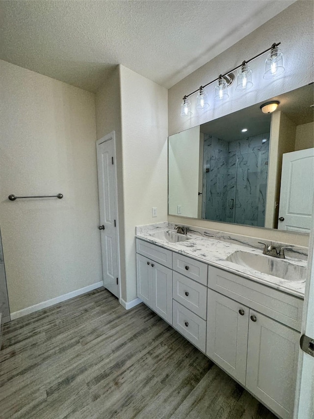 bathroom with wood finished floors, a sink, a marble finish shower, and double vanity