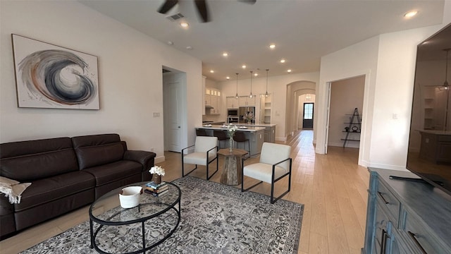 living room with ceiling fan, light wood-style floors, arched walkways, baseboards, and visible vents