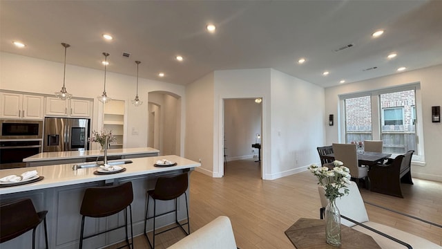 kitchen featuring visible vents, arched walkways, light wood-type flooring, a sink, and stainless steel appliances
