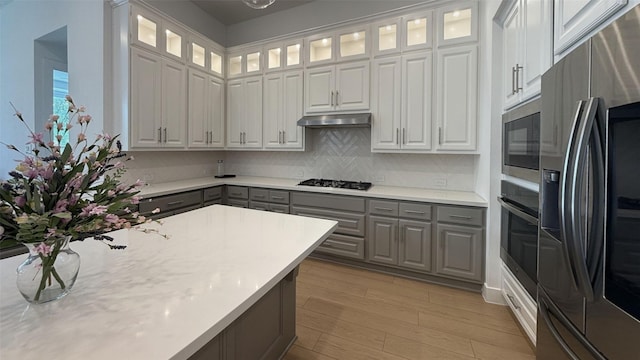 kitchen with light wood-type flooring, gray cabinetry, light countertops, under cabinet range hood, and stainless steel appliances