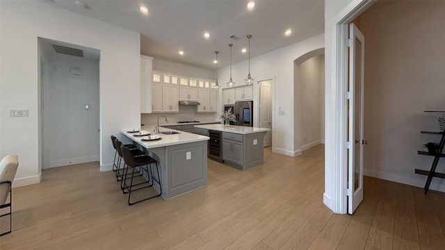 kitchen with a kitchen breakfast bar, arched walkways, light countertops, stainless steel fridge with ice dispenser, and light wood-style flooring