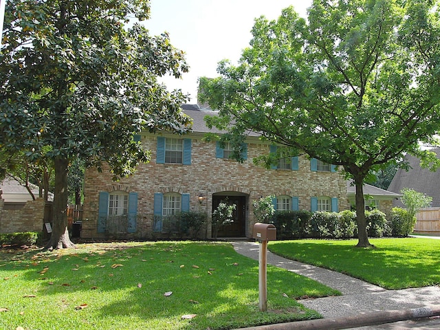 colonial inspired home featuring fence, brick siding, and a front yard