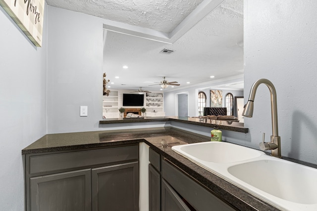 bar featuring a sink, a textured ceiling, visible vents, a ceiling fan, and a fireplace