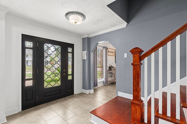 entryway with stairs, a textured ceiling, light tile patterned floors, arched walkways, and ornamental molding