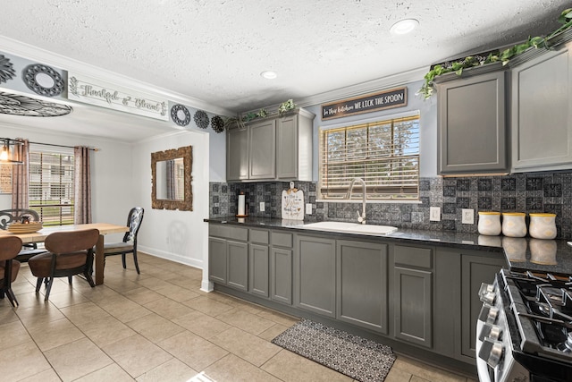 kitchen with dark countertops, a sink, decorative backsplash, stainless steel gas stove, and gray cabinetry