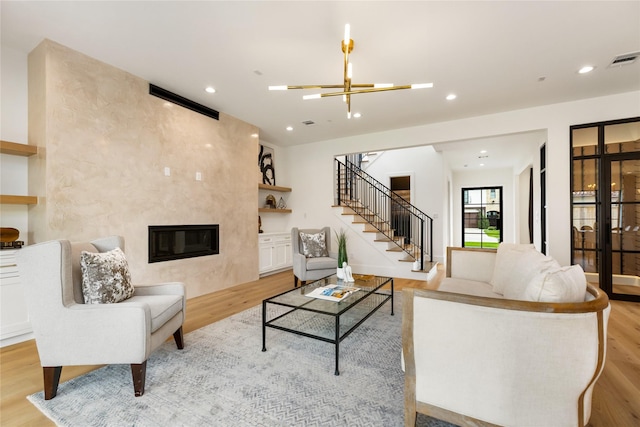 living room with a chandelier, light wood finished floors, visible vents, a fireplace, and stairs