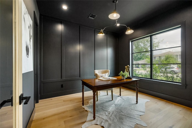 office space with a decorative wall, visible vents, and light wood-type flooring
