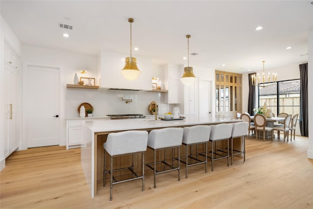 kitchen with white cabinets, light wood-style flooring, a spacious island, a notable chandelier, and light countertops