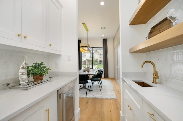 kitchen featuring light wood-style flooring, a sink, white cabinetry, open shelves, and light stone countertops