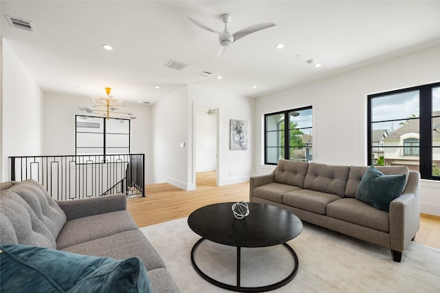 living area featuring visible vents, light wood finished floors, and ceiling fan with notable chandelier