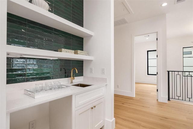 bar featuring a sink, baseboards, light wood-style floors, decorative backsplash, and indoor wet bar