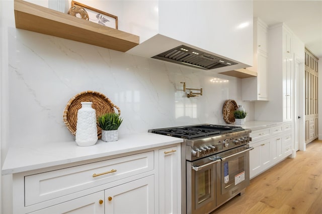kitchen featuring wall chimney exhaust hood, light wood-style flooring, backsplash, white cabinetry, and range with two ovens
