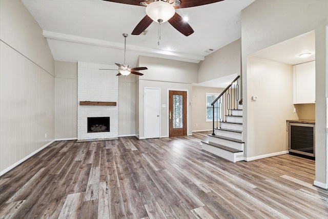 unfurnished living room featuring stairway, a brick fireplace, wood finished floors, and ceiling fan