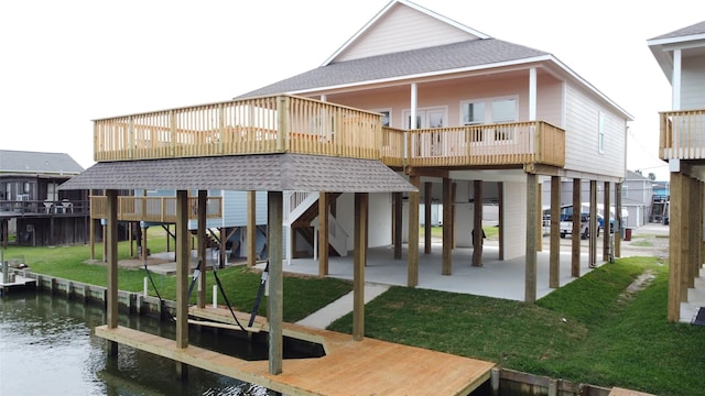 rear view of house featuring a deck with water view, a lawn, and roof with shingles