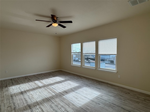 unfurnished room with baseboards, wood finished floors, visible vents, and a ceiling fan