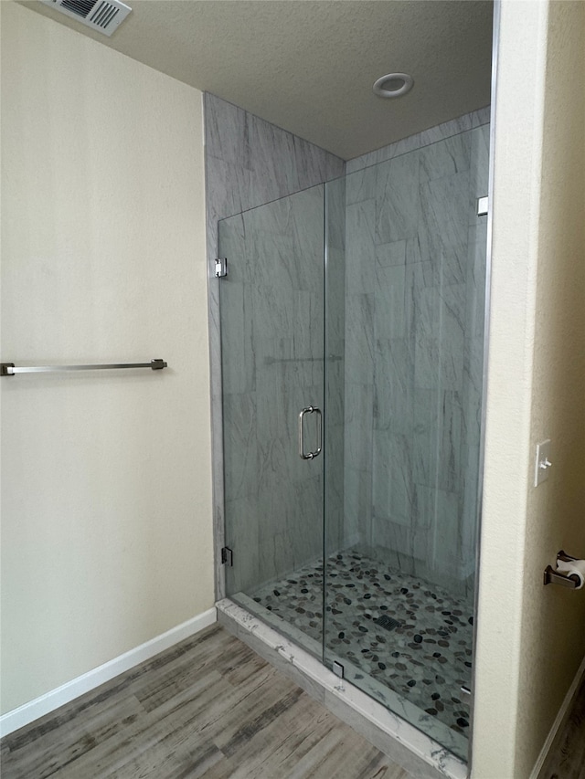 bathroom with wood finished floors, visible vents, baseboards, and a marble finish shower