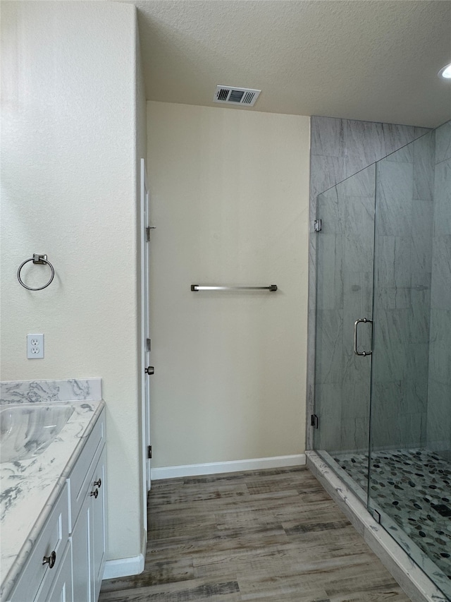 full bathroom featuring wood finished floors, a marble finish shower, a textured ceiling, vanity, and baseboards