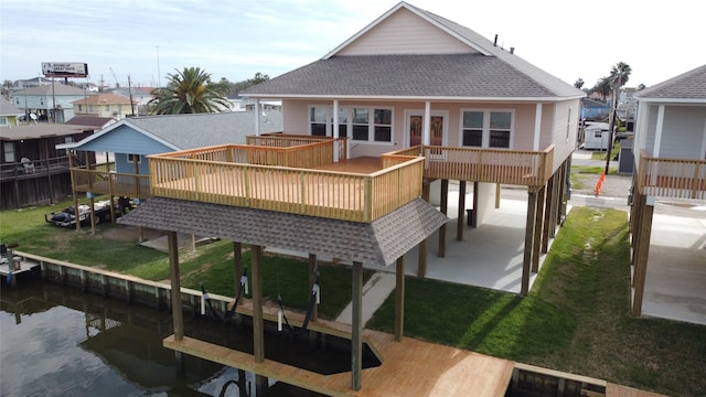 back of house with a deck with water view, roof with shingles, and a yard