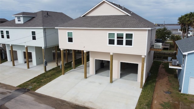rear view of house with a carport, central air condition unit, concrete driveway, an attached garage, and a shingled roof