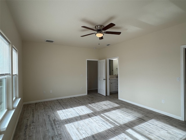 unfurnished bedroom with wood finished floors, visible vents, baseboards, ceiling fan, and ensuite bathroom