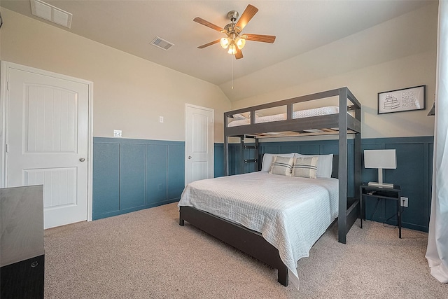 carpeted bedroom with a wainscoted wall, visible vents, and vaulted ceiling