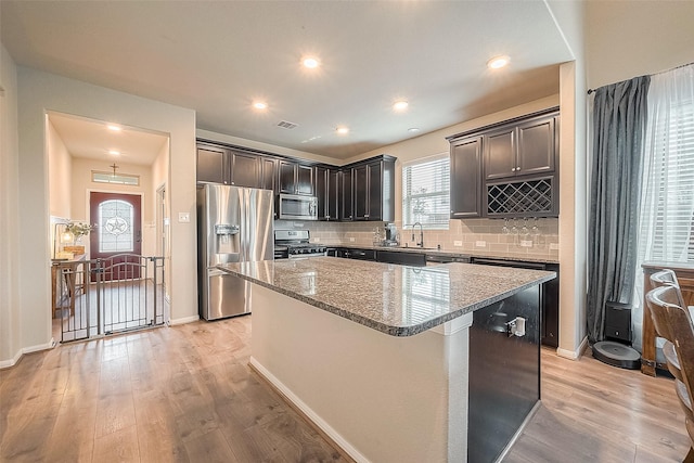 kitchen featuring light wood finished floors, stainless steel appliances, a sink, light stone countertops, and a center island
