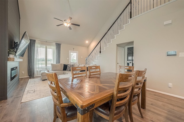 dining area featuring stairway, wood finished floors, a fireplace, high vaulted ceiling, and ceiling fan
