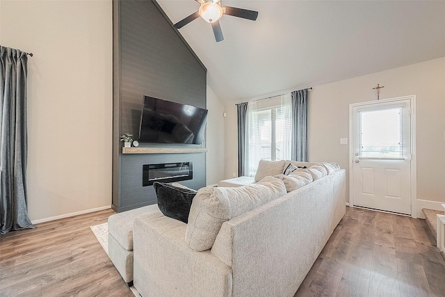 living area featuring vaulted ceiling, a ceiling fan, light wood-style floors, a fireplace, and baseboards