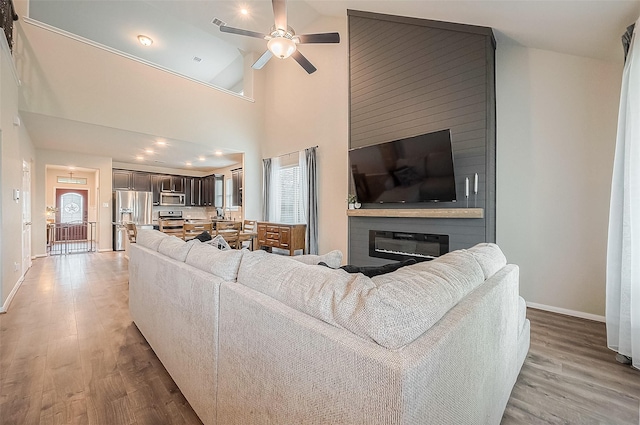 living area with a ceiling fan, a large fireplace, light wood finished floors, baseboards, and recessed lighting