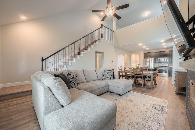 living area featuring light wood-style flooring, baseboards, a ceiling fan, stairs, and high vaulted ceiling