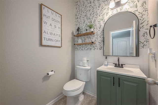 bathroom with wallpapered walls, toilet, vanity, and wainscoting
