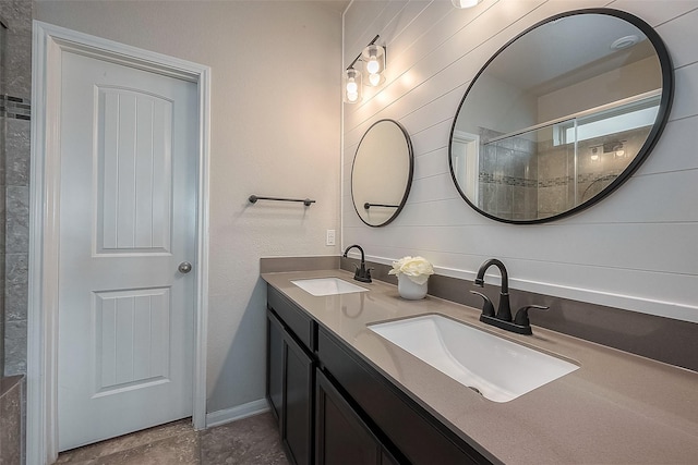 full bath featuring baseboards, a sink, double vanity, and a tile shower