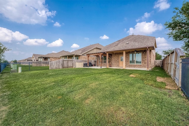 rear view of house with roof with shingles, a fenced backyard, brick siding, a patio area, and a lawn