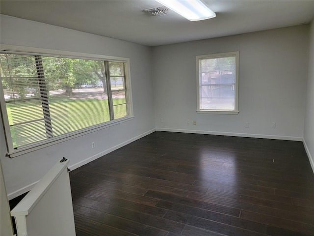 spare room featuring dark wood finished floors, plenty of natural light, and baseboards