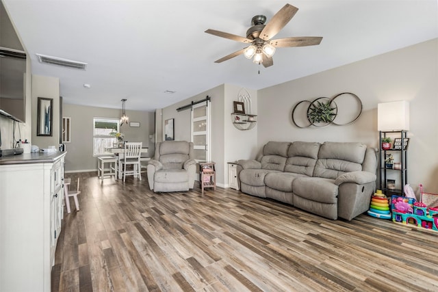 living area featuring ceiling fan, a barn door, baseboards, wood finished floors, and visible vents