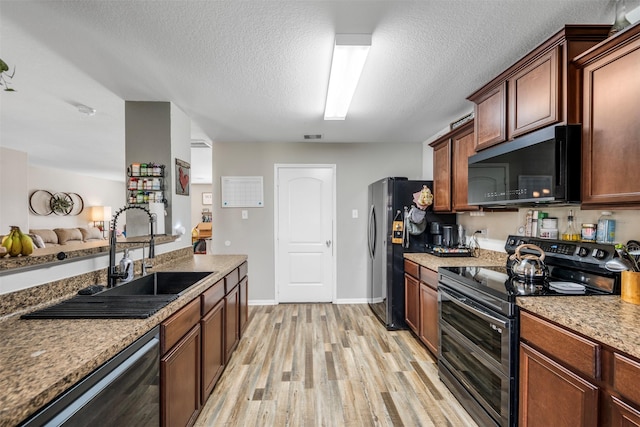 kitchen with baseboards, a textured ceiling, a sink, light wood-style flooring, and appliances with stainless steel finishes
