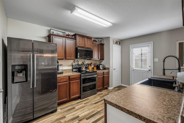 kitchen with dark countertops, a sink, a textured ceiling, stainless steel appliances, and light wood-type flooring
