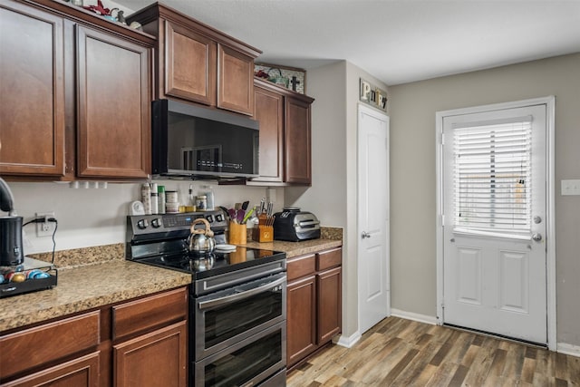 kitchen with wood finished floors, black microwave, baseboards, light countertops, and range with two ovens