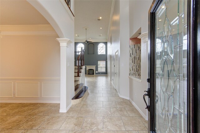 entrance foyer featuring arched walkways, decorative columns, stairs, ceiling fan, and crown molding