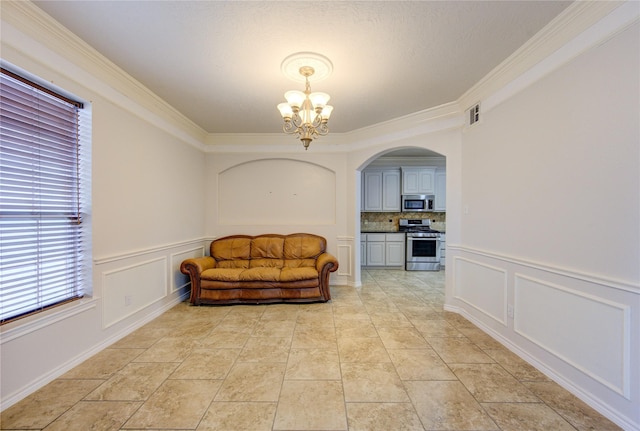 living area with a wainscoted wall, arched walkways, a chandelier, a decorative wall, and ornamental molding