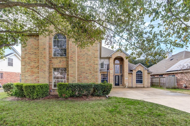 traditional home featuring fence, a front lawn, and brick siding