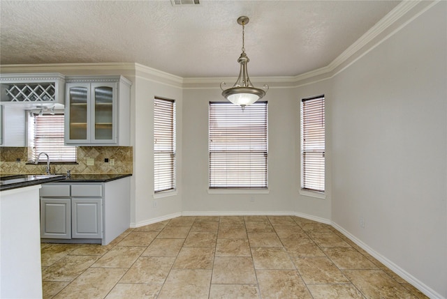 kitchen featuring dark countertops, decorative backsplash, glass insert cabinets, decorative light fixtures, and ornamental molding