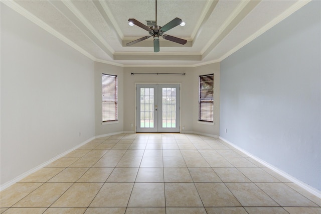 empty room with a ceiling fan, light tile patterned floors, french doors, a tray ceiling, and ornamental molding