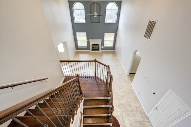 stairway with baseboards, a ceiling fan, a high ceiling, and a fireplace