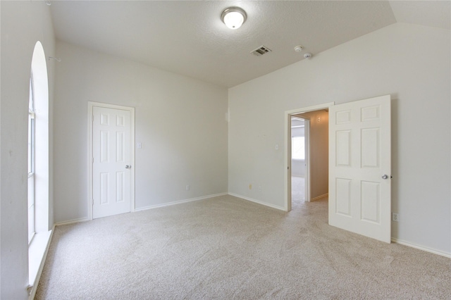 unfurnished room with light carpet, vaulted ceiling, visible vents, and baseboards